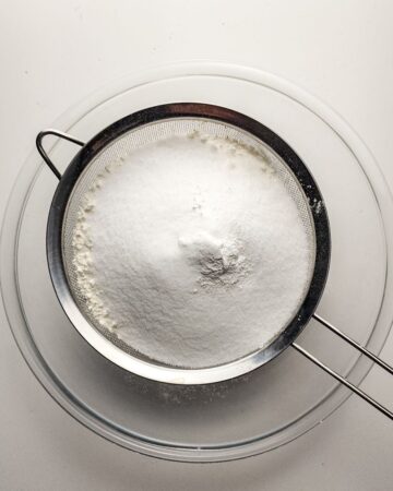 Flour, sugar, baking powder, baking soda being sifted to make the dry ingredients for a lemon bundt cake.