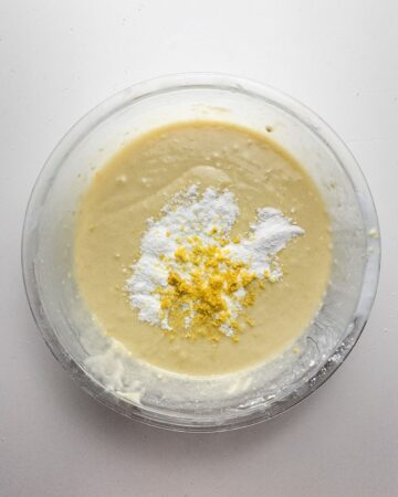 A glass mixing bowl with cake batter, lemon pudding mix, and lemon zest mixed together for a bundt cake.