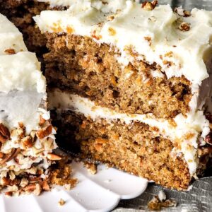 Homemade carrot cake recipe with cream cheese frosting and a slice being picked up from the cake.