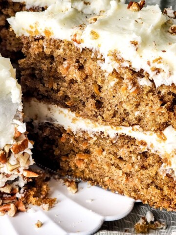 Homemade carrot cake recipe with cream cheese frosting and a slice being picked up from the cake.