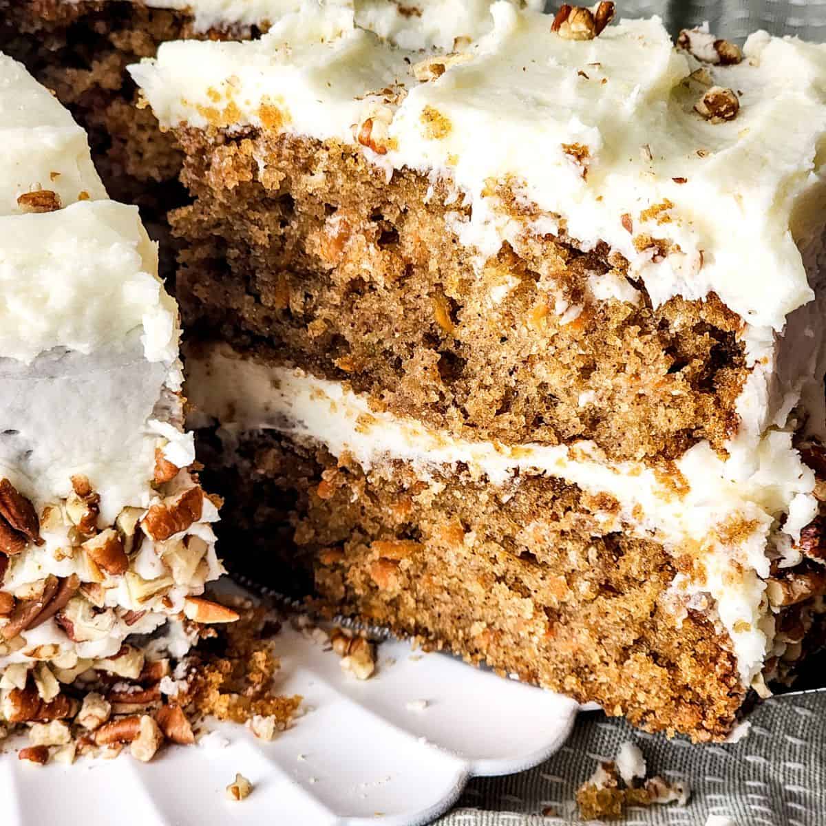 Homemade carrot cake recipe with cream cheese frosting and a slice being picked up from the cake.