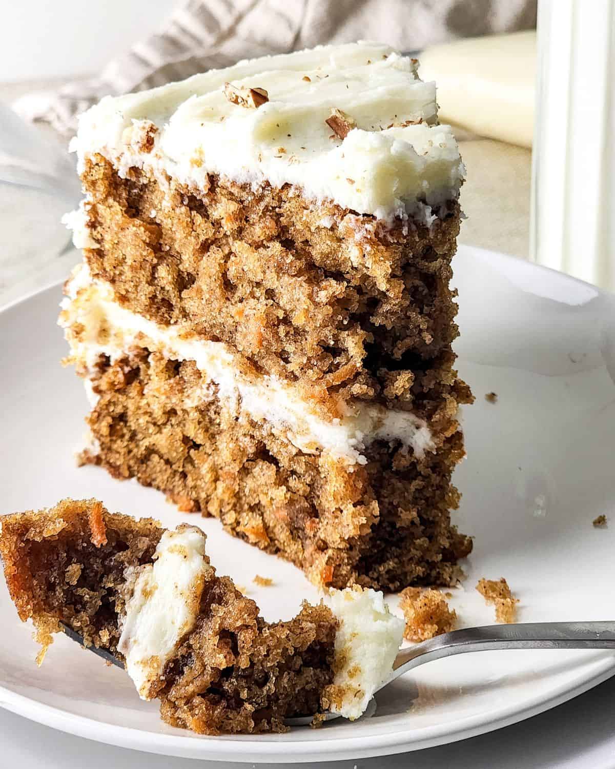 A slice of layered carrot cake with cream cheese frosting on a plate.