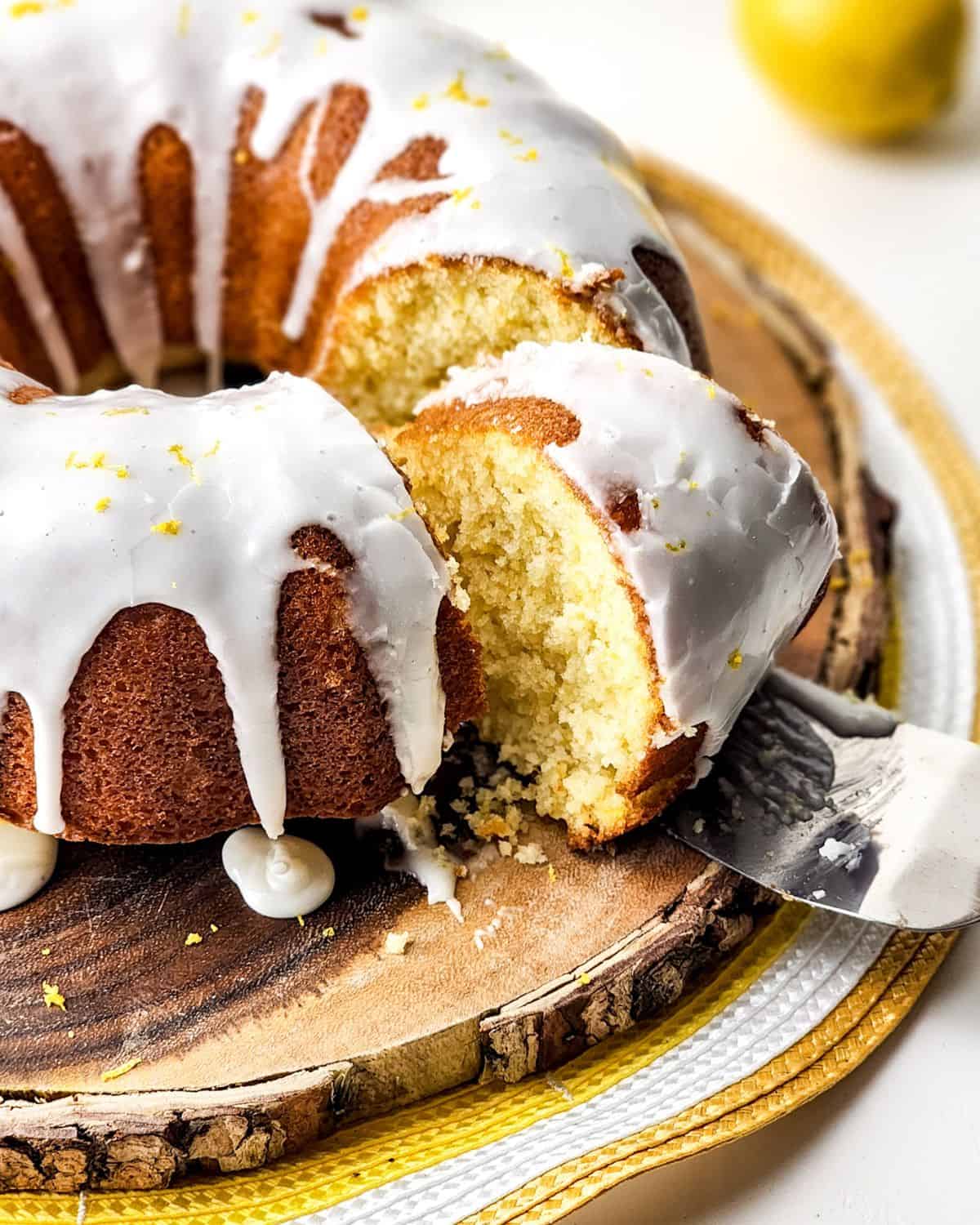 Homemade lemon bundt cake glazed and a slice being cut.