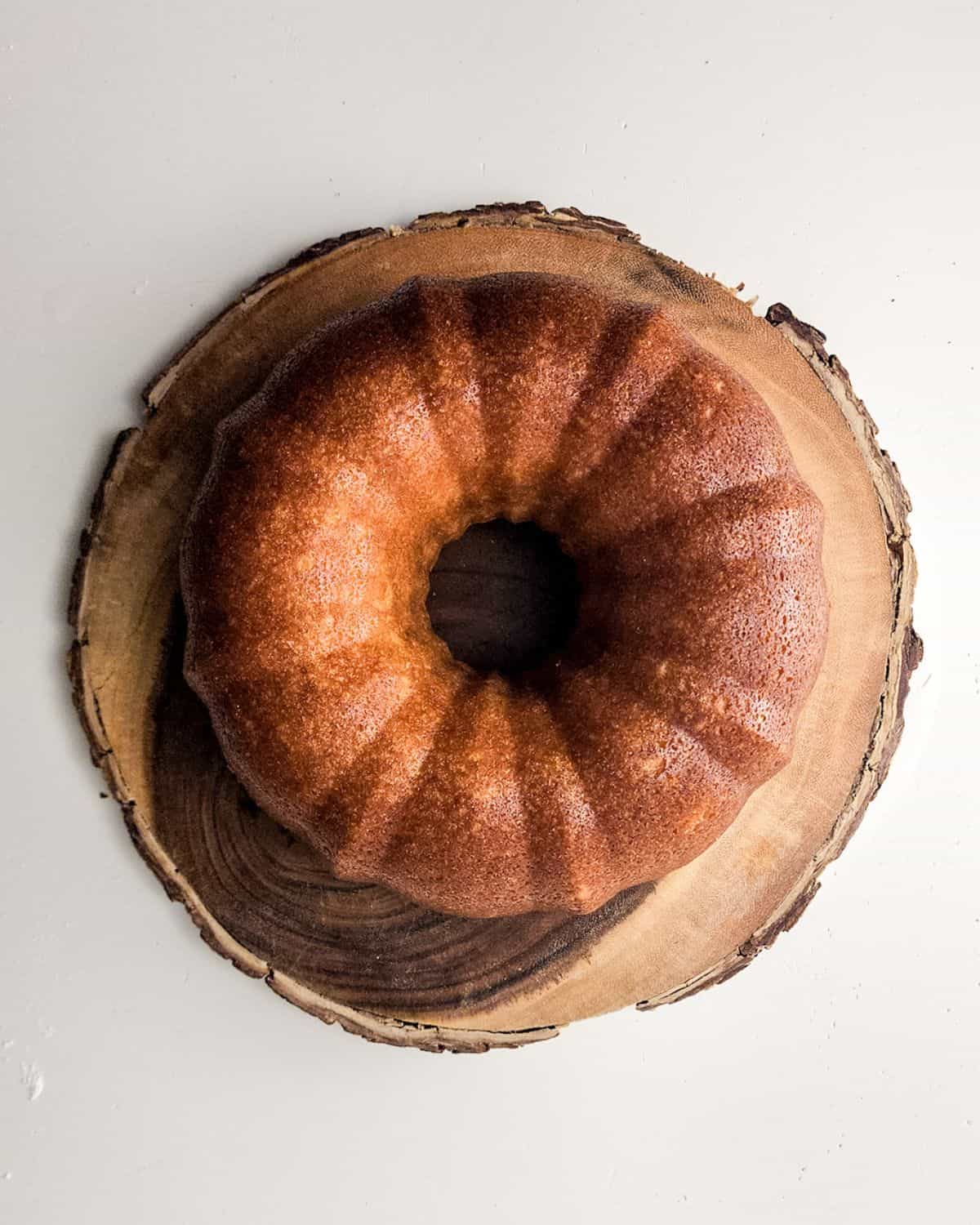 A lemon bundt cake on a wooden platter that has been baked and cooled.