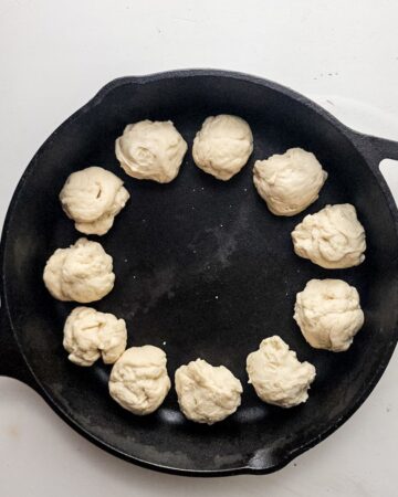 A cast iron pan with pizza dough rolled into balls to begin a pizza dip. 