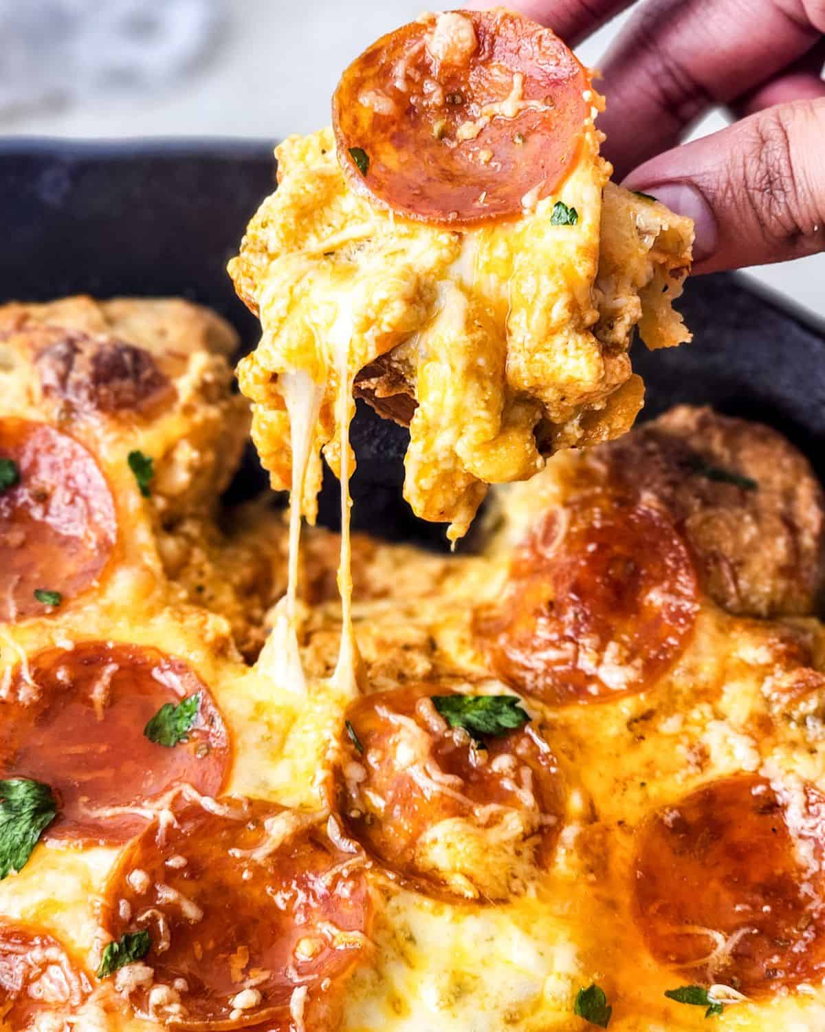 Pizza dip with pepperoni being lifted up out of a cast iron pan.