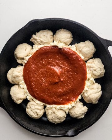 A cast iron skillet with pizza dough balls and a center of cheese to make a pizza dip.