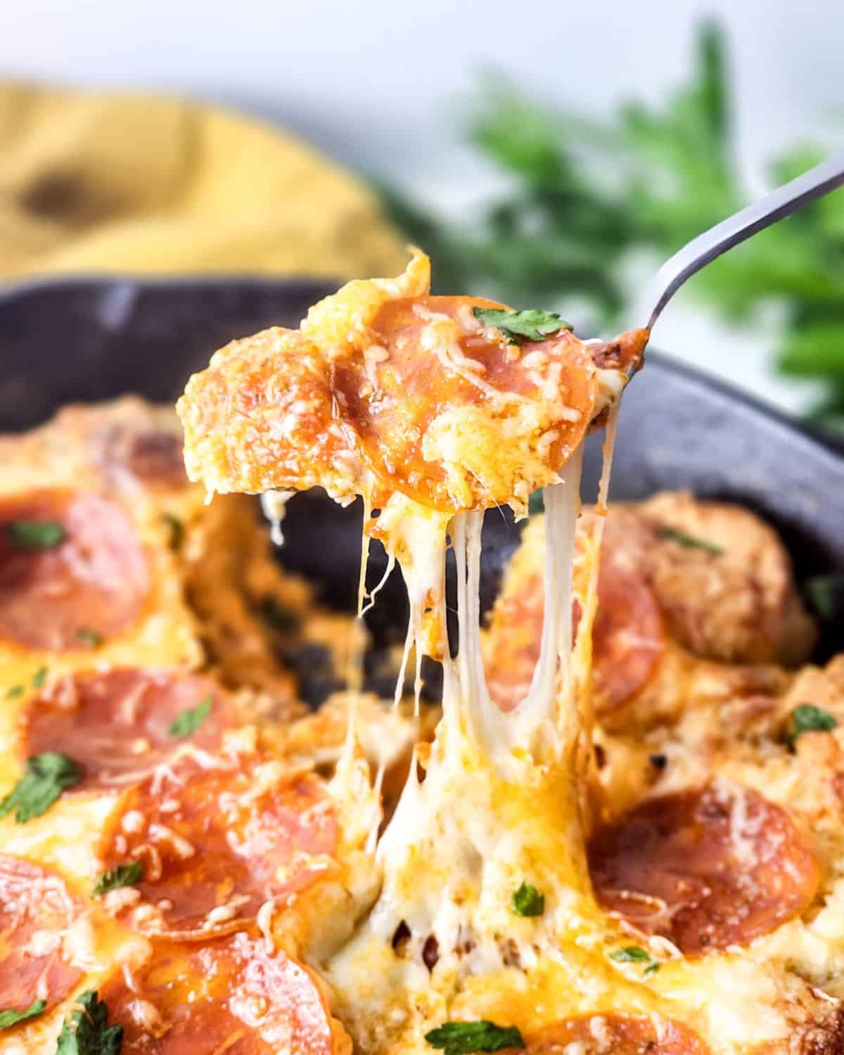 Cast iron skillet pizza dip with pepperoni being picked up out of the pan.