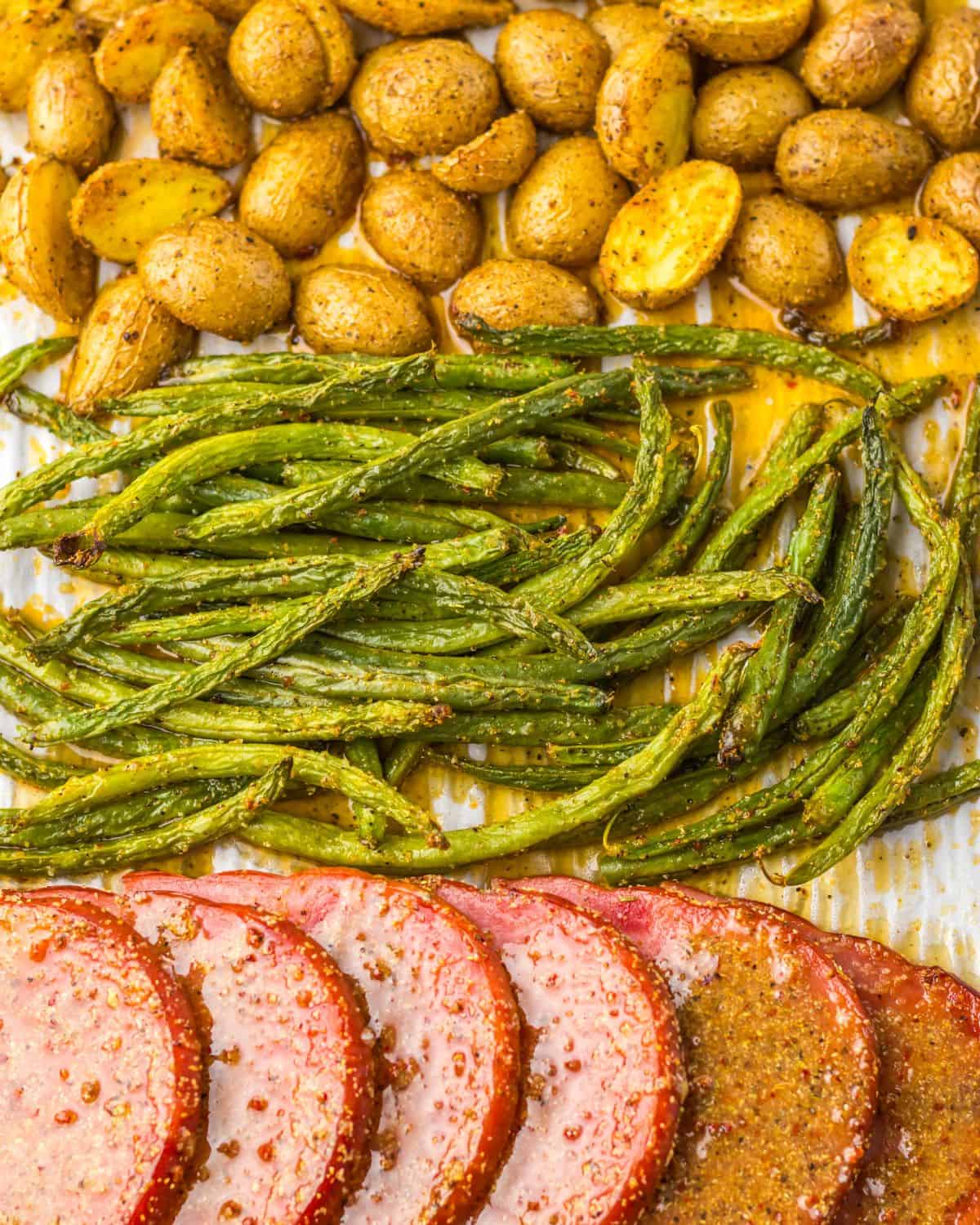 A sheet pan dinner of sliced ham, potatoes, and green beans. 