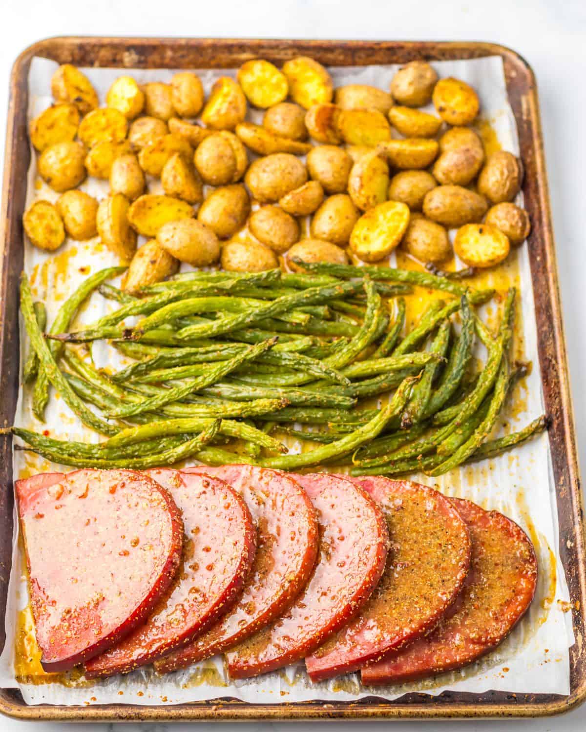 A sheet pan ham dinner with potatoes and green beans.