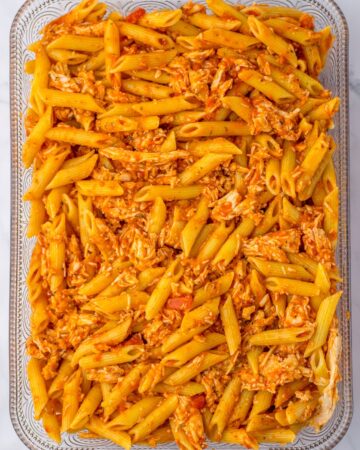 Glass baking dish with cooked pasta, chicken, and marinara sauce to make chicken parm pasta.