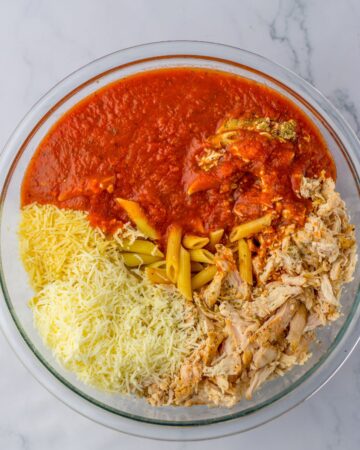 A large mixing bowl with cooked pasta, chicken, cheee to make a chicken parm pasta recipe.