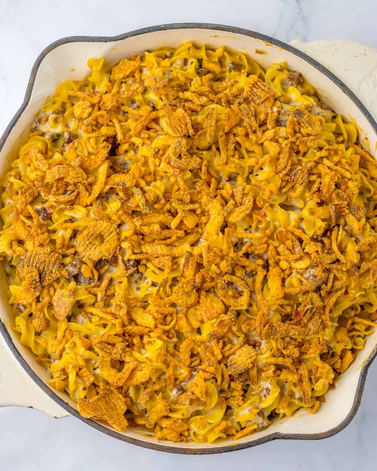 A large white saute pan with egg noodles in a creamy French onion sauce topped with crispy french onions.