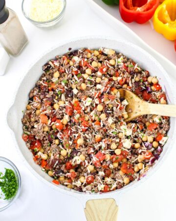 A saute pan with ground beef, rice, feta cheese, and roasted red peppers to make stuffed peppers with greek flavors. 