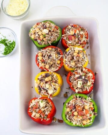 Bell peppers stuffed with greek flavors in a baking pan.