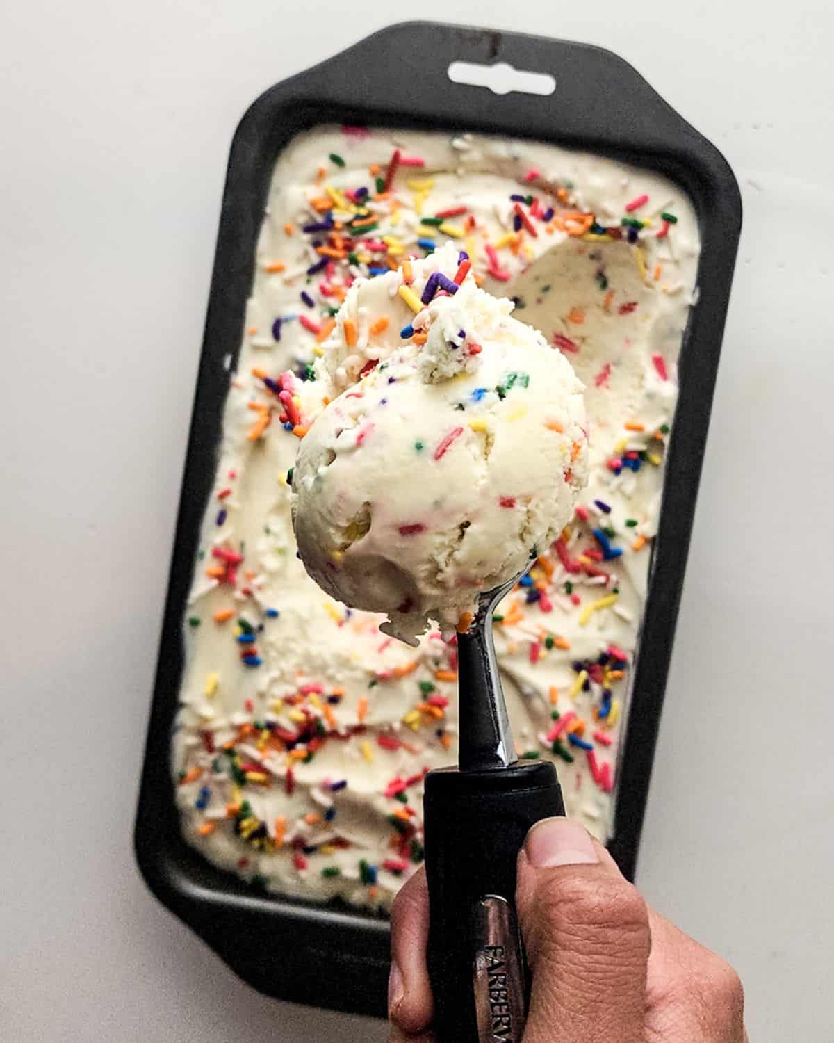 No-Churn Homemade Birthday Cake Ice Cream in a loaf pan being scooped out for serving. 
