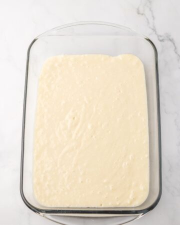 A glass rectangle baking pan with white cake batter to make a poke cake.