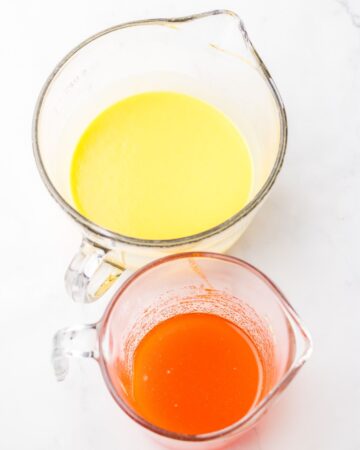 Two measuring cups one with orange gelatin and hot water. The second measuring jar has milk and vanilla pudding for an orange creamsicle poke cake.