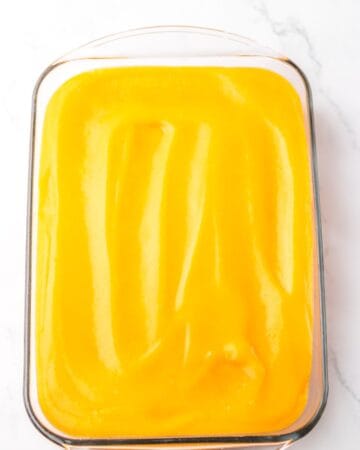 A rectangle baking dish with a baked vanilla cake with poked holes and topped with orange creamsicle mixture for an orange poke cake.