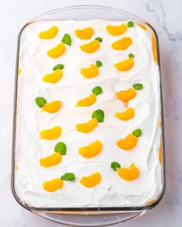 A 9 x13-inch orange creamsicle poke cake topped with mandarin orange slices and mint.