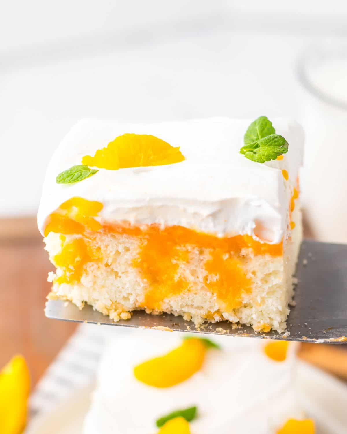 A slice or orange creamsicle poke cake being picked up topped with whipped cream, mandarin orange wedge and mint.
