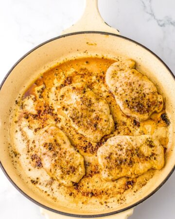 Boneless pork chops browned in a pan to make pork chops and potatoes in a garlic honey sauce.