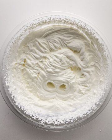 A glass bowl with heavy cream whipped to make no churn ice cream.
