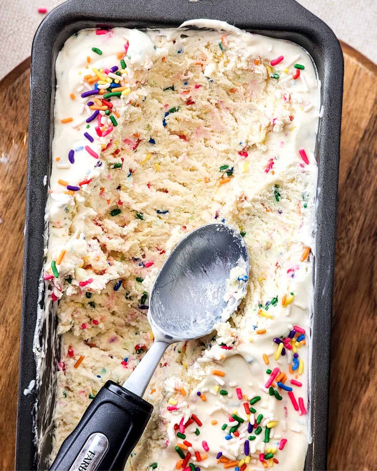 No churn birthday cake ice cream being scooped out of a loaf pan.
