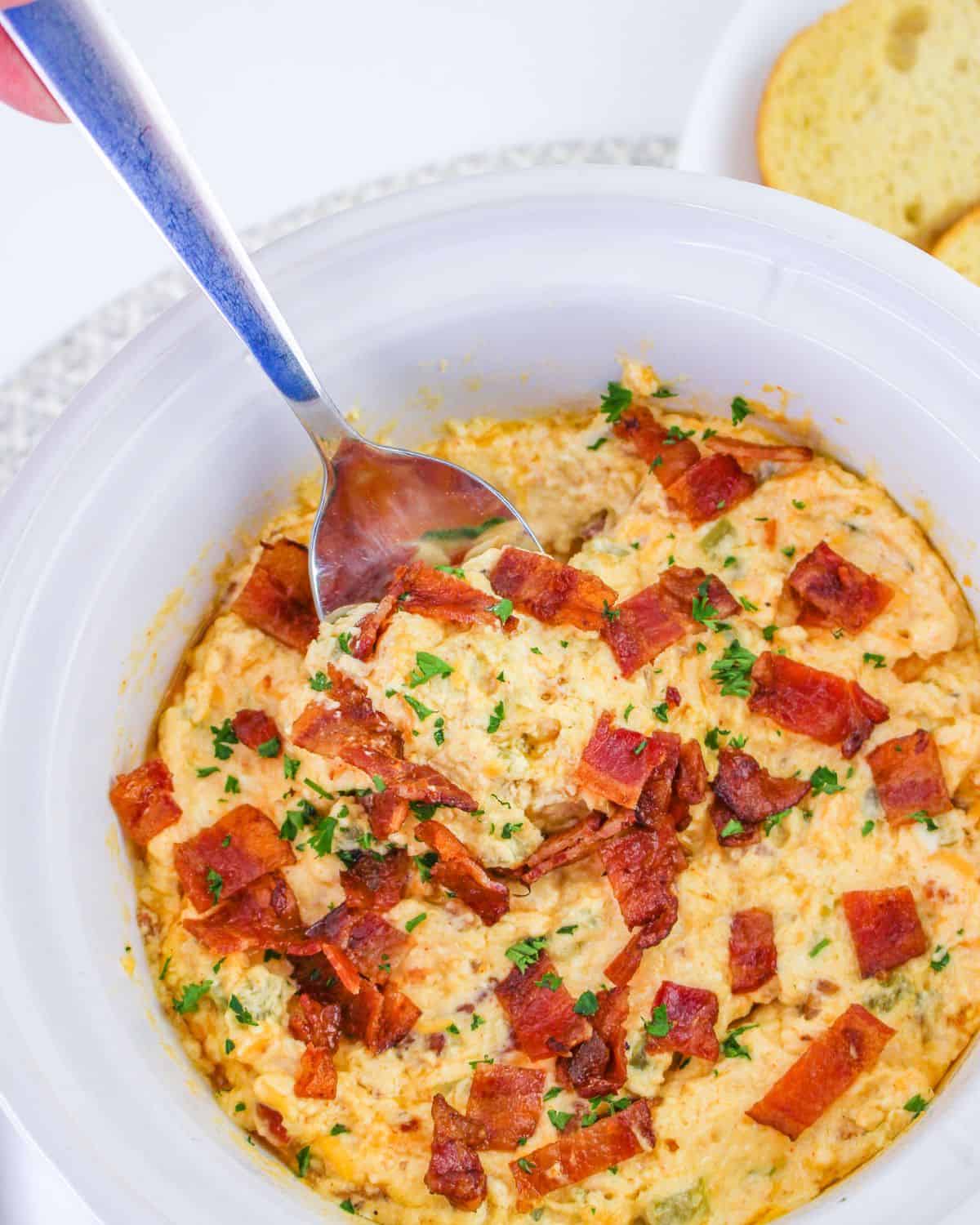 Jalapeno popper dip with chopped bacon in a white slow cooker.