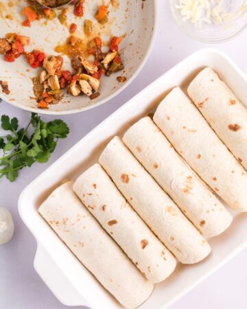 Flour tortillas rolled and filled with Mexican spiced seasoned chicken in a large casserole pan. 
