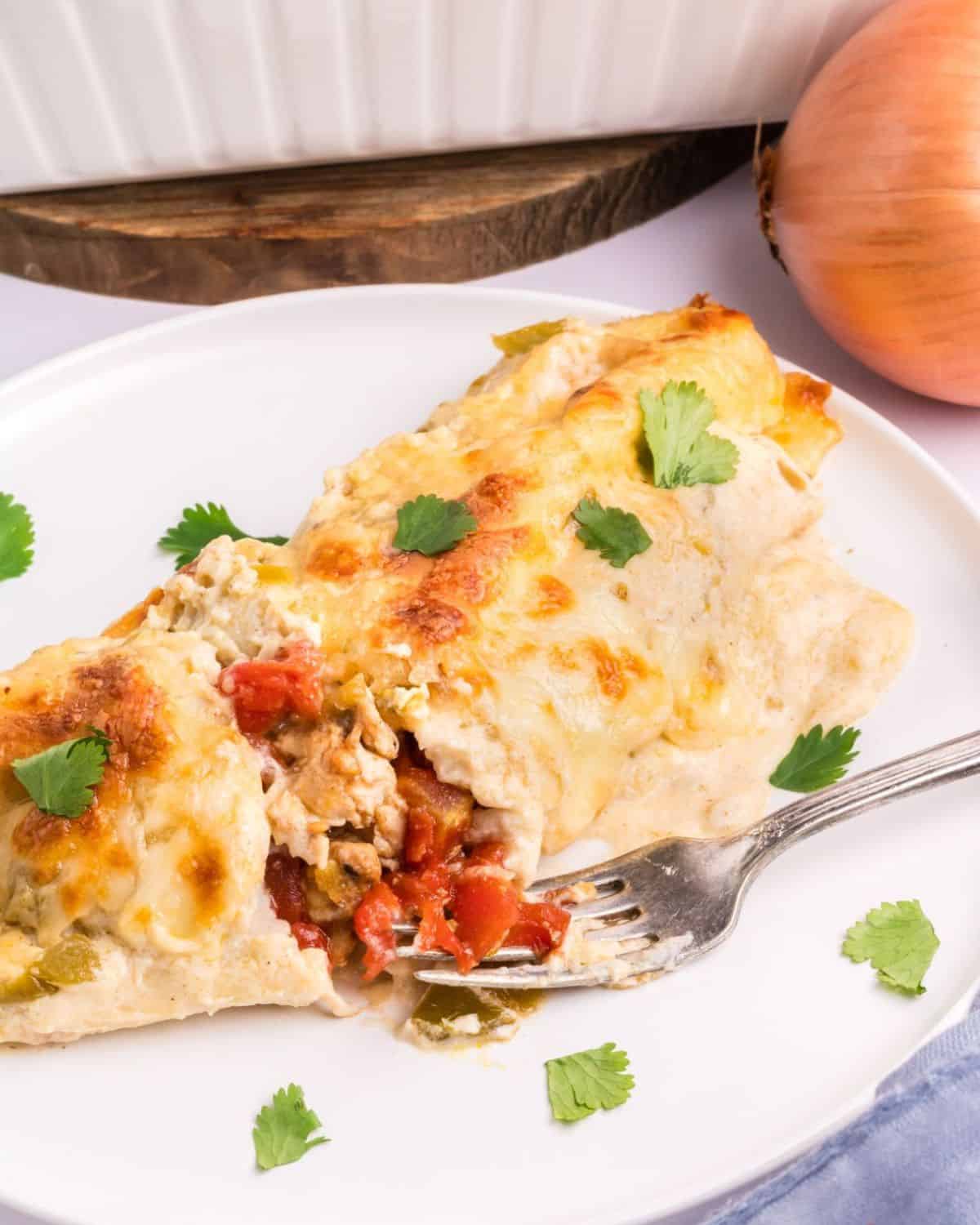 Sour cream chicken enchilada cut in half on a white plate.