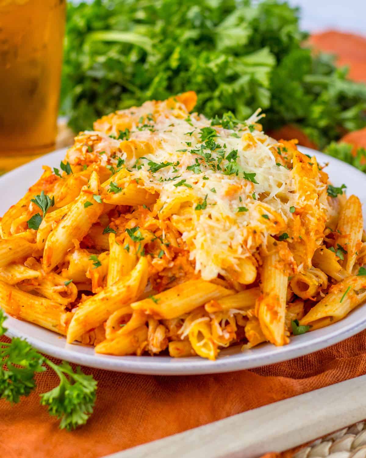 Chicken parm pasta on a plate topped with cheese and chopped parsley.