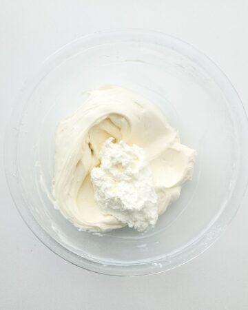 Process shot of a glass bowl with whipped cream being added to a cream cheese mix for no bake cheesecake stuffed waffle cones.