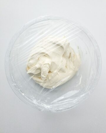 A cheesecake mousse in a glass bowl covered with plastic wrap to make stuffed cheesecake waffle cones.