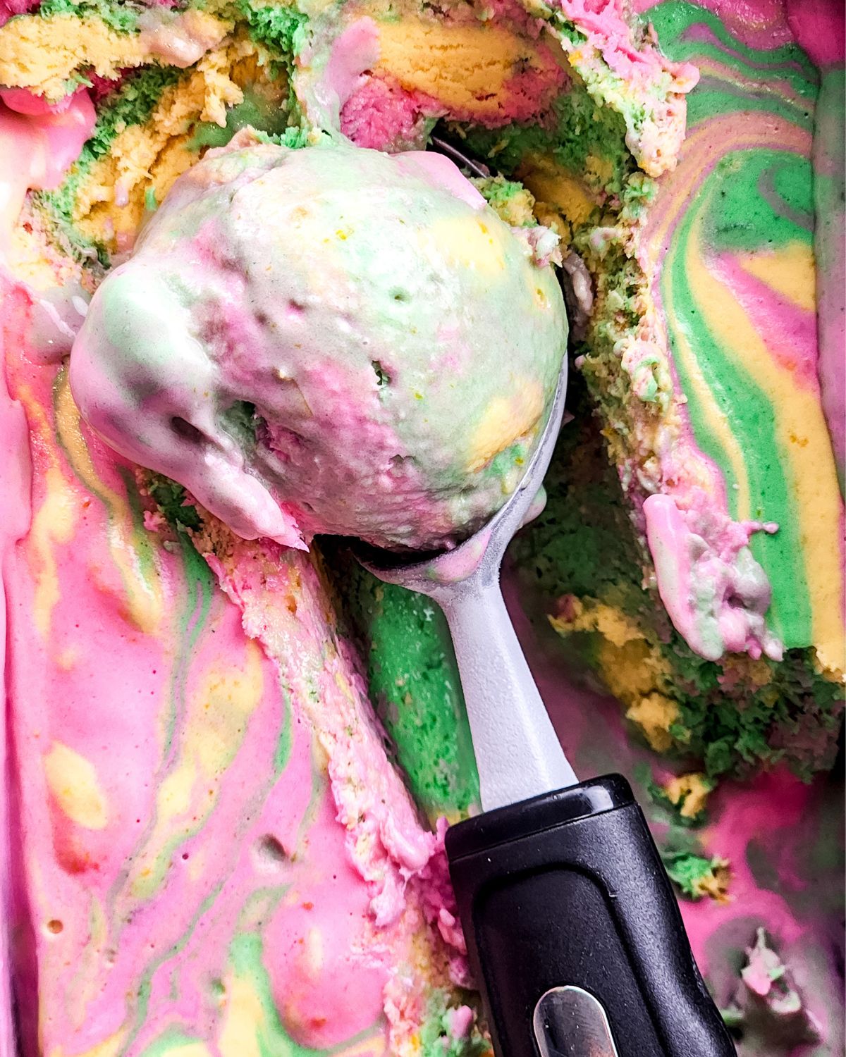 An ice cream scoop n a bowl of rainbow sherbet ice cream.