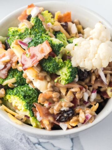 Broccoli and cauliflower salad with chopped bacon and sunflower seeds and raisins in a creamy sauce.