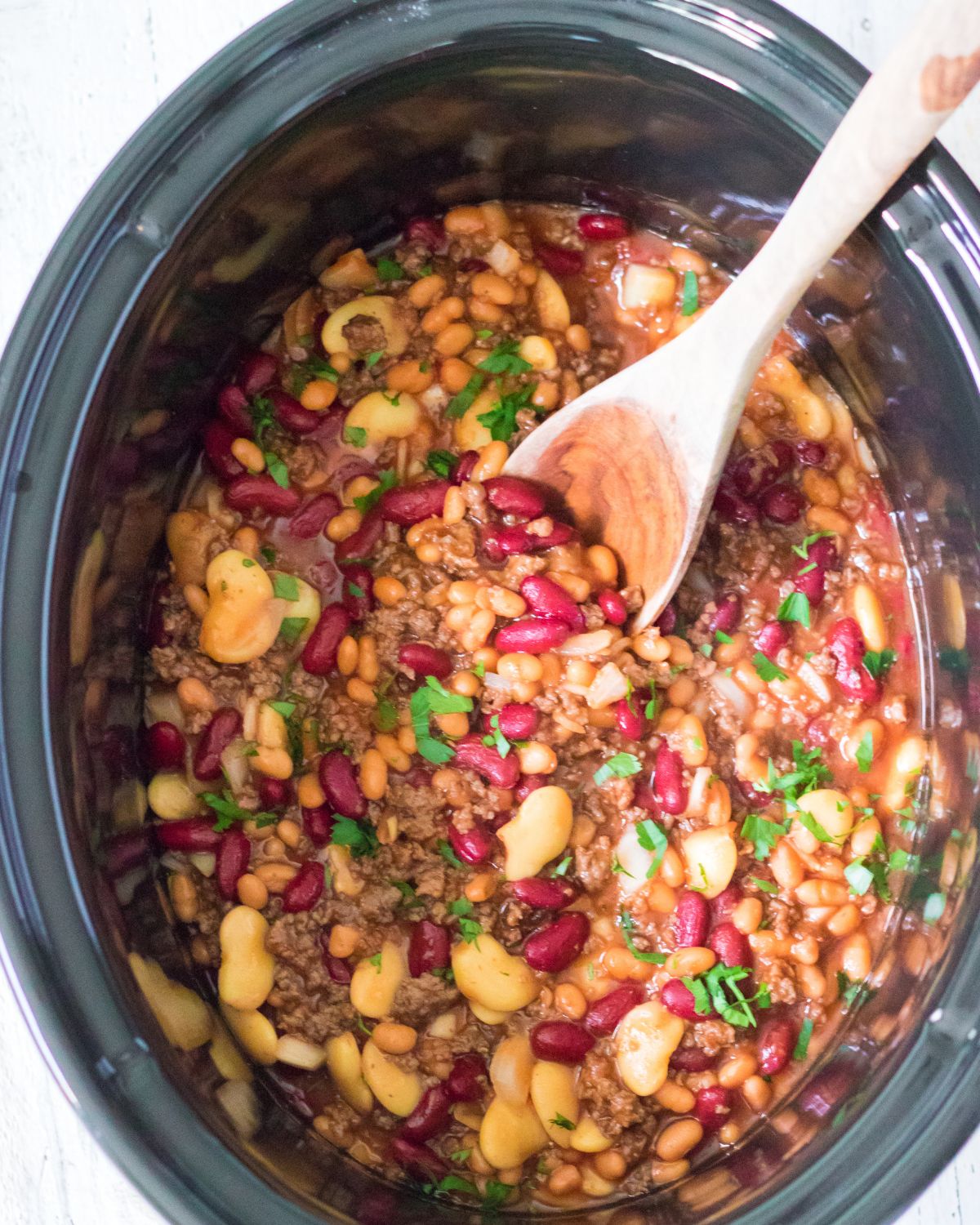 A slow cooker with pork and beans, butter beans, kidney beans, and ground beef to make cowboy beans.