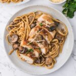 A white plate with fetuccini, chicken marsala and mushrooms.