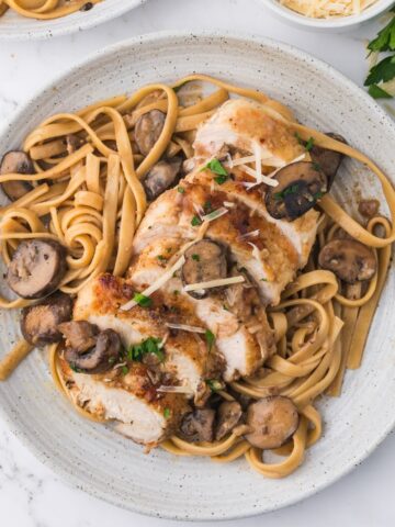 A white plate with fetuccini, chicken marsala and mushrooms.