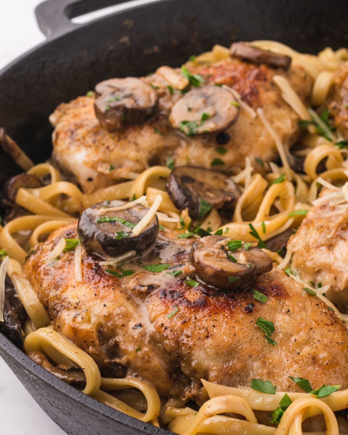 Chicken marsala pasta with mushrooms in a cast iron pan.