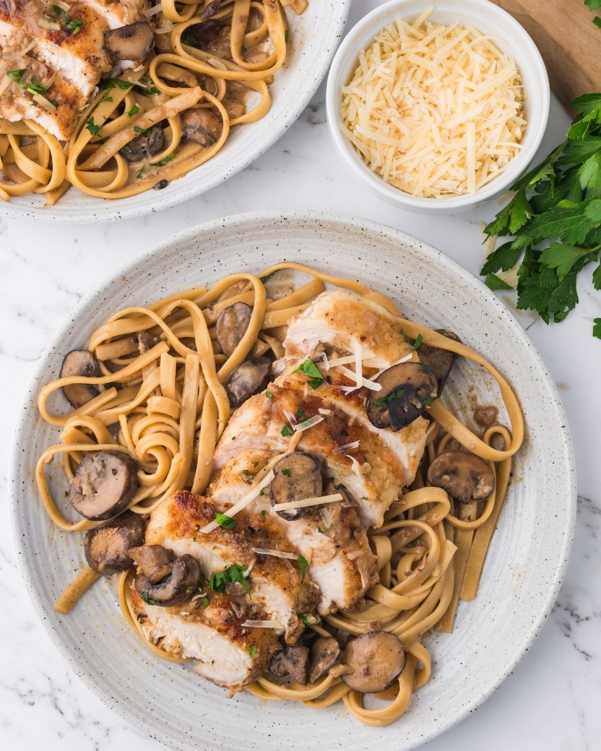Sliced chicken breasts in a marsala sauce over fettuccine on a white plate.
