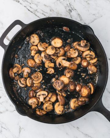 Mushrooms in a cast iron pan that have been sauteed in butter.