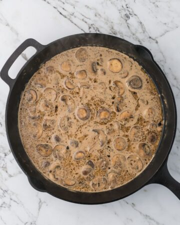 A cast iron pan with heavy cream, chicken broth, mushrooms, and marsala wine to make the sauce for chicken marsala over fettuccine.