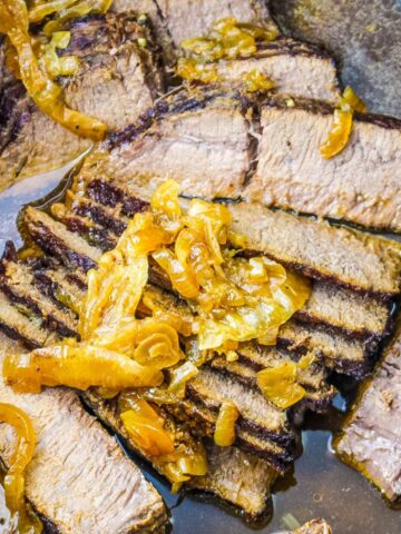 A slow cooker with sliced flank steak topped with carmelized onions.