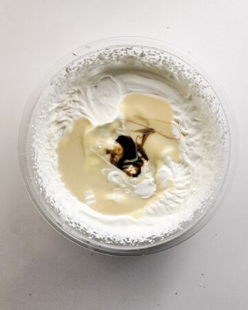 A glass bowl with whipped heavy cream, sweetened condensed milk, vanilla bean paste, and salt to make cookie monster ice cream.