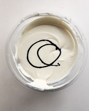 A glass bowl with the ingredients to make cookie monster ice cream with blue food gel mixed in to the heavy cream.
