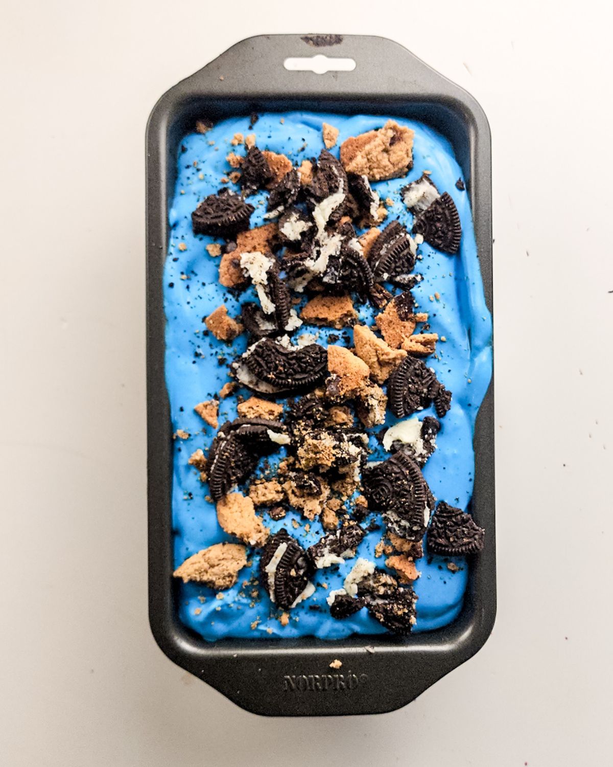 Cookie Monster Ice cream topped with chopped cookies in a loaf pan.