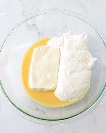 A glass bowl with eggs, cream cheese to make a no bake strawberry pie.
