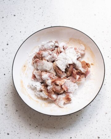 A bowl of marinated pork strips in cornstarch to make a pork chop suey recipe.