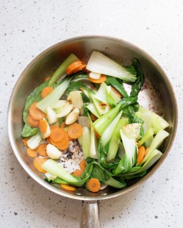 A saute pan with bok choy, carrots, and garlic.